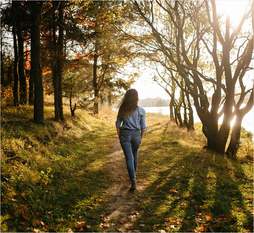 A woman walking alone along a sunlit woodland path