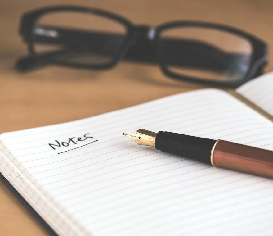 An open notebook marked “Notes” beside a pen and reading glasses
