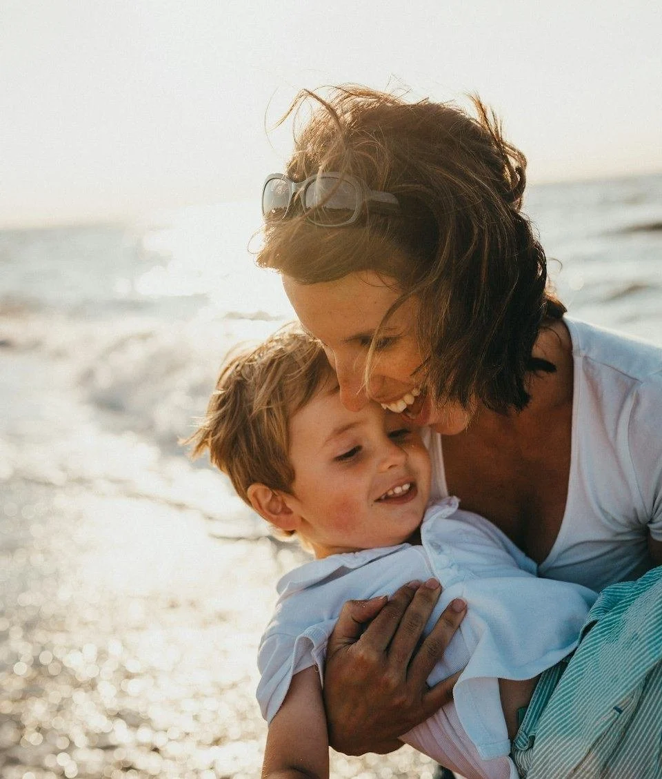 A mother and her young son laughing together on a sunlit beach