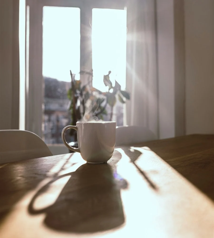 A steaming cup on a wooden table in a quiet, sunlit room, a moment to pause and rest