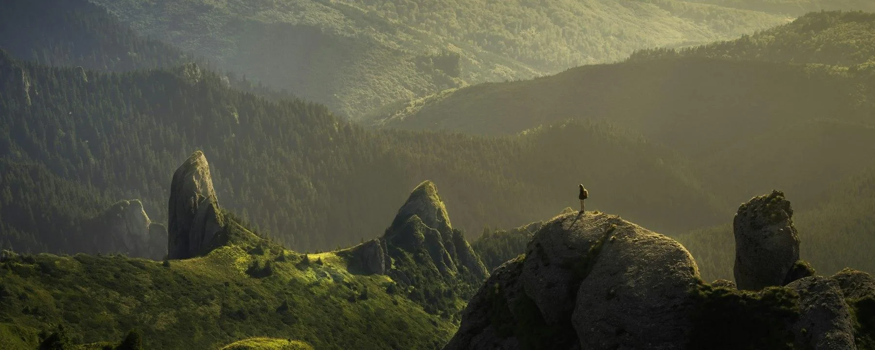 A small figure standing on a rocky outcrop above a misty green valley